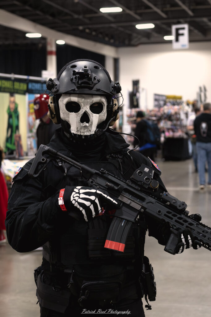 "Cosplayer dressed as Ghost from Call of Duty, wearing a tactical skull mask, military-style gear, and carrying weapons, standing confidently in an urban environment."